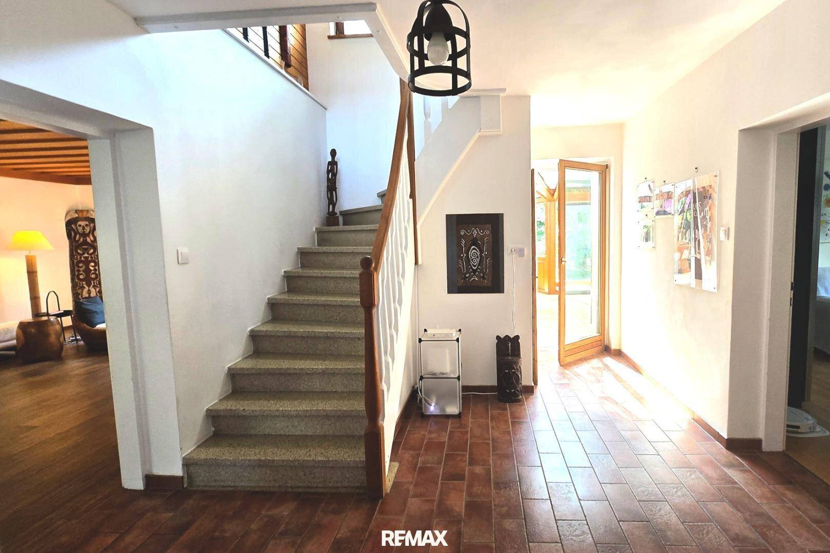 Heller Eingangsbereich mit Steintreppe, Holzgeländer und Terrakotta-Fliesenboden.