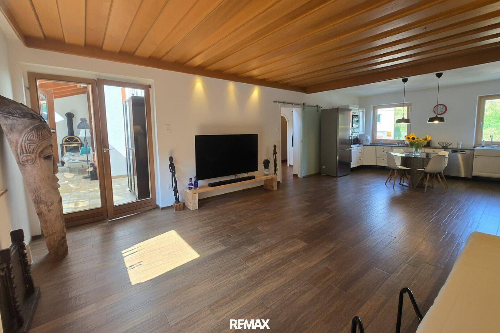 Geräumiger offener Wohnbereich mit Holzbalkendecke, Fliesenboden und Zugang zur Terrasse.
