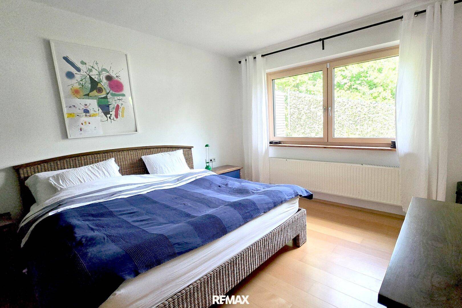 Helles Schlafzimmer mit Doppelbett, Holzboden und großem Fenster mit Blick ins Grüne.