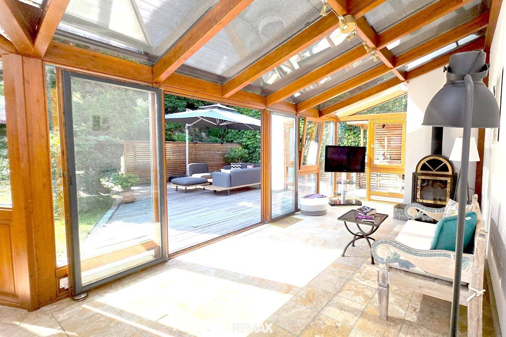 Geräumiger Wintergarten mit Wohnbereich, Kamin und großen Glasfronten zur Terrasse.