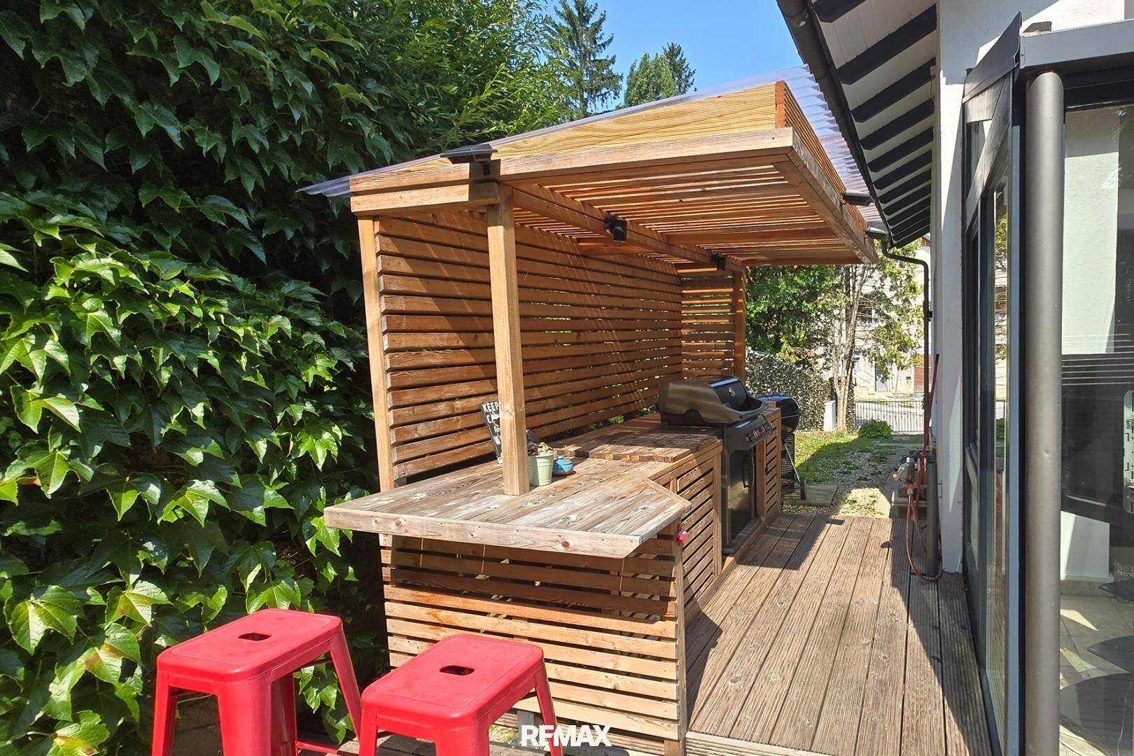Überdachte Außenküche mit Grillbereich und Barhockern auf der Holzterrasse.