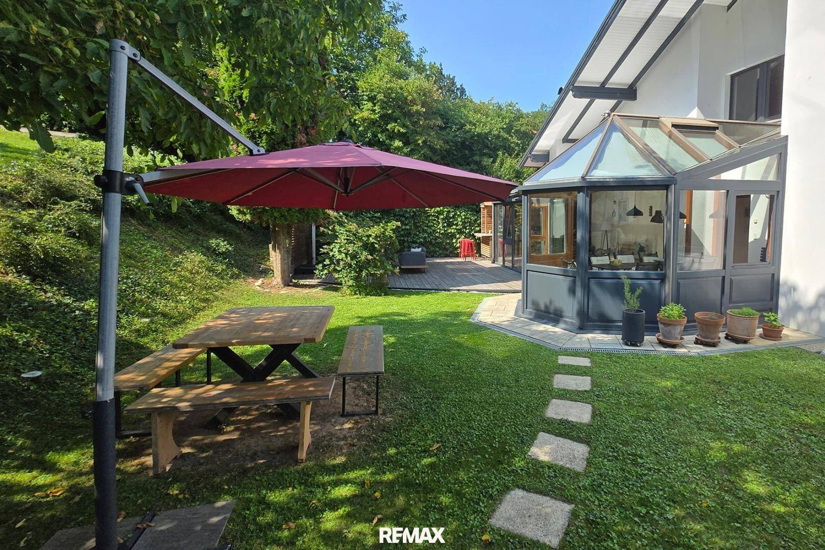 Gepflegter Gartenbereich mit Picknicktisch, Sonnenschirm und angrenzendem Wintergarten.
