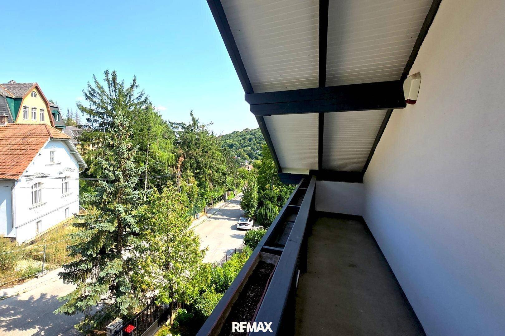 Schmaler, überdachter Balkon mit Blick auf die Straße und umliegende Häuser.