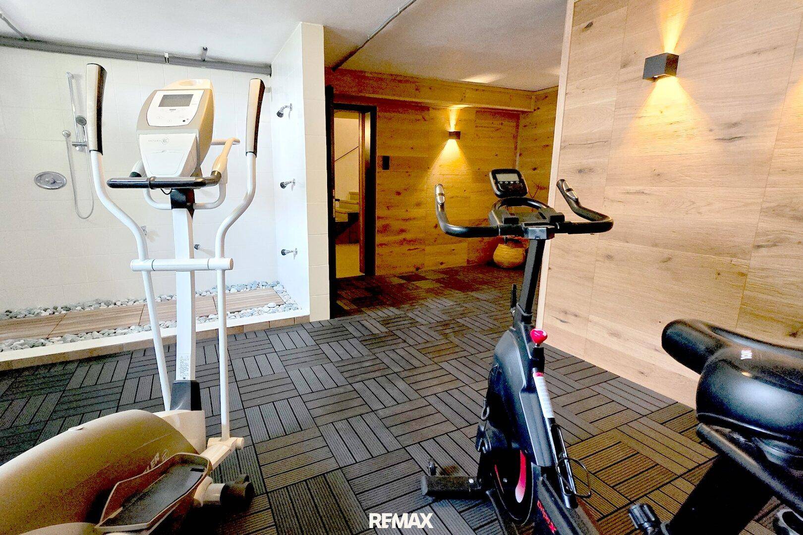 Moderner Fitnessbereich mit Trainingsgeräten und angrenzendem Duschbereich in Holzoptik.