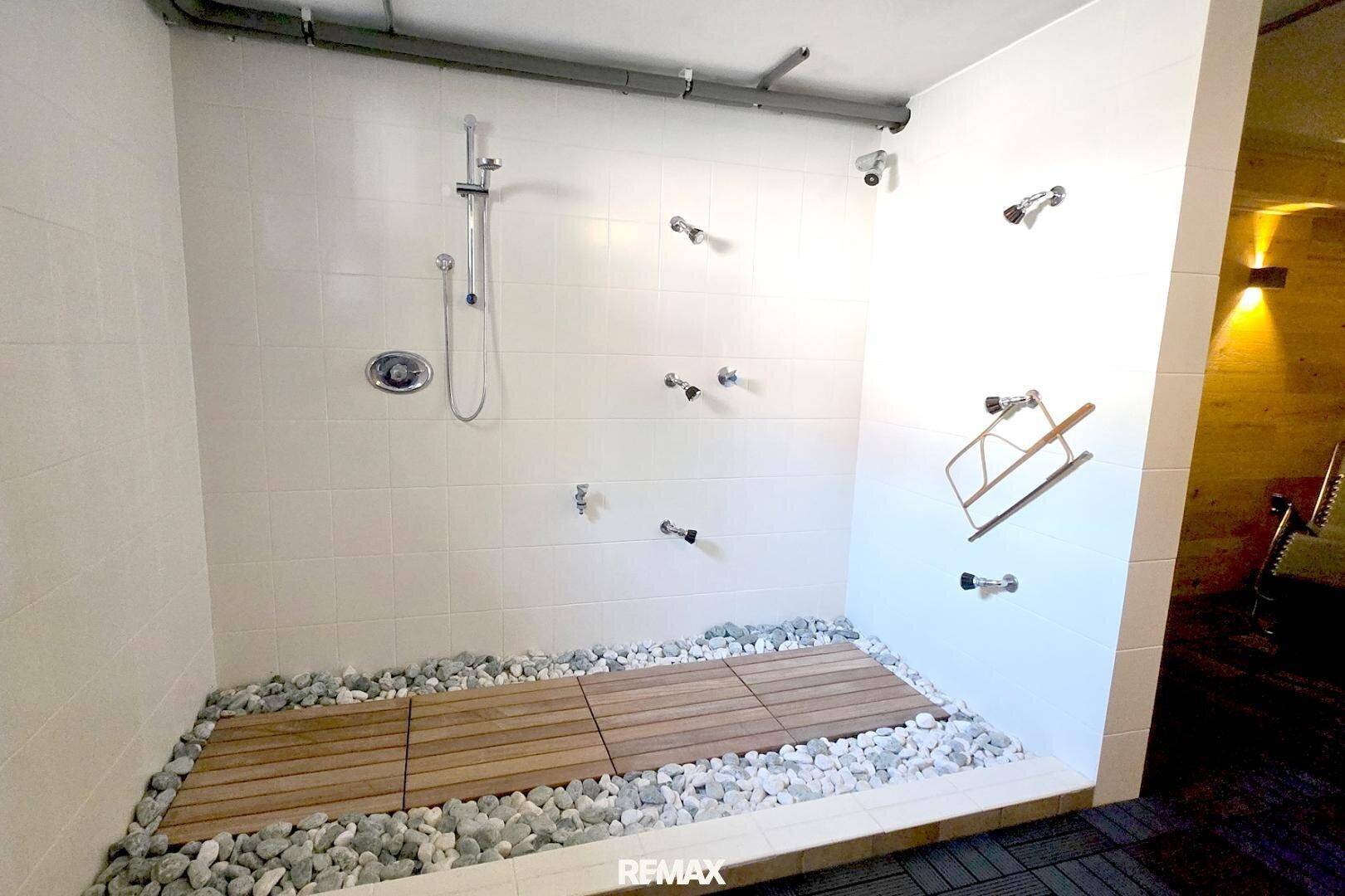 Geräumiger Duschbereich mit mehreren Duschköpfen und einem Boden aus Holz und Kieselsteinen.