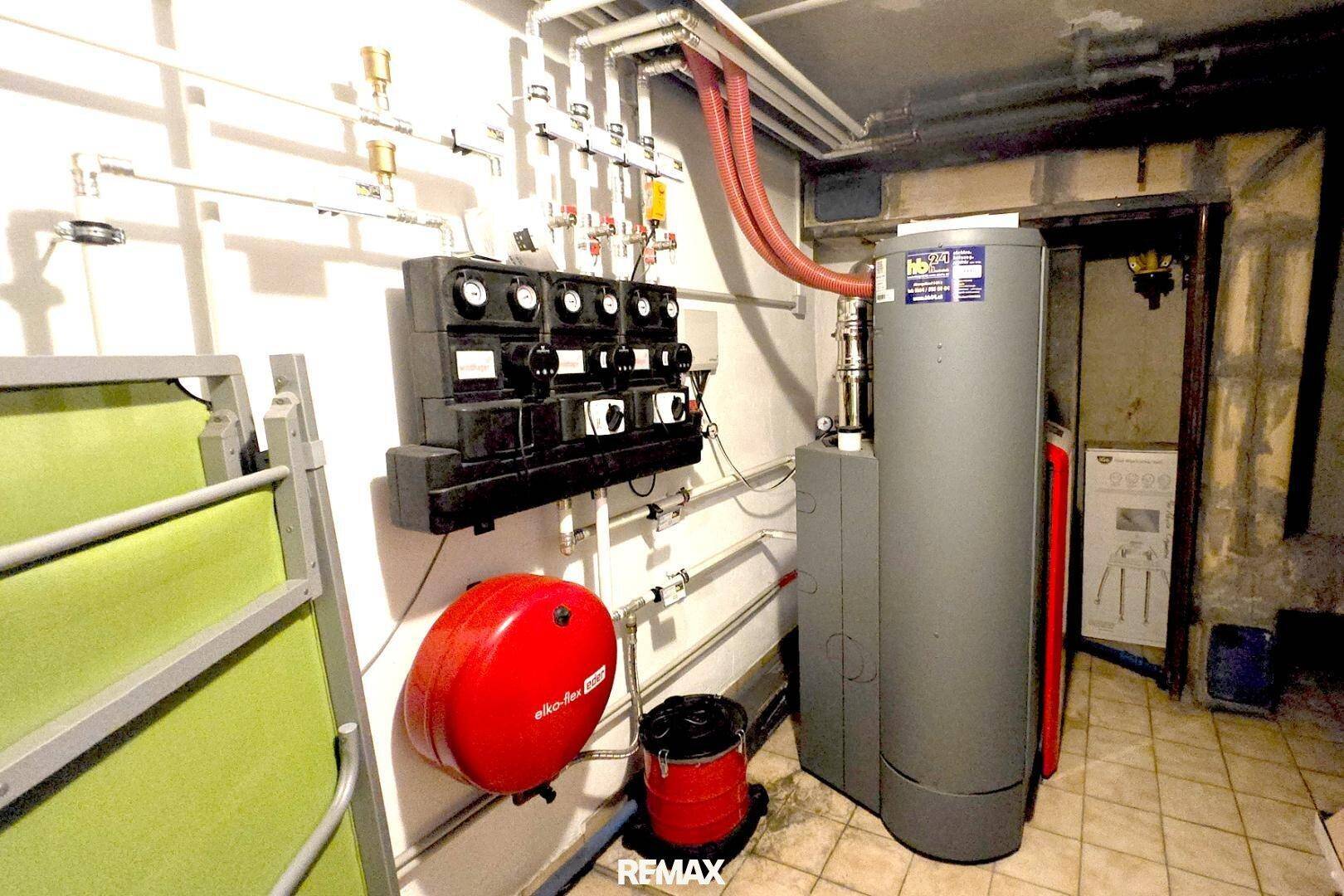 Technikraum im Keller mit Warmwasserbereiter, Rohren und elektrischen Installationen.