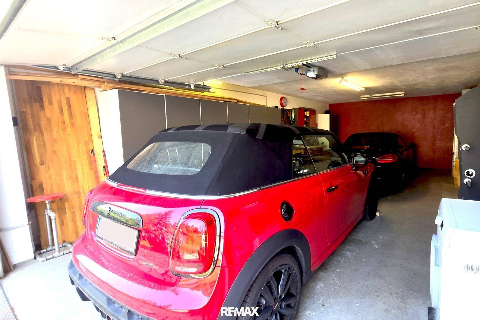 Geräumige Garage mit zwei geparkten Autos, Lagerschränken und roter Akzentwand.