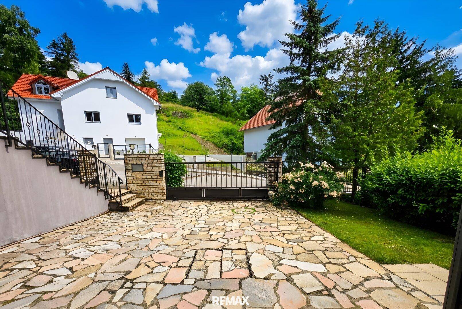 Großer gepflasterter Vorplatz mit Natursteinplatten und einem Einfahrtstor vor dem Haus.