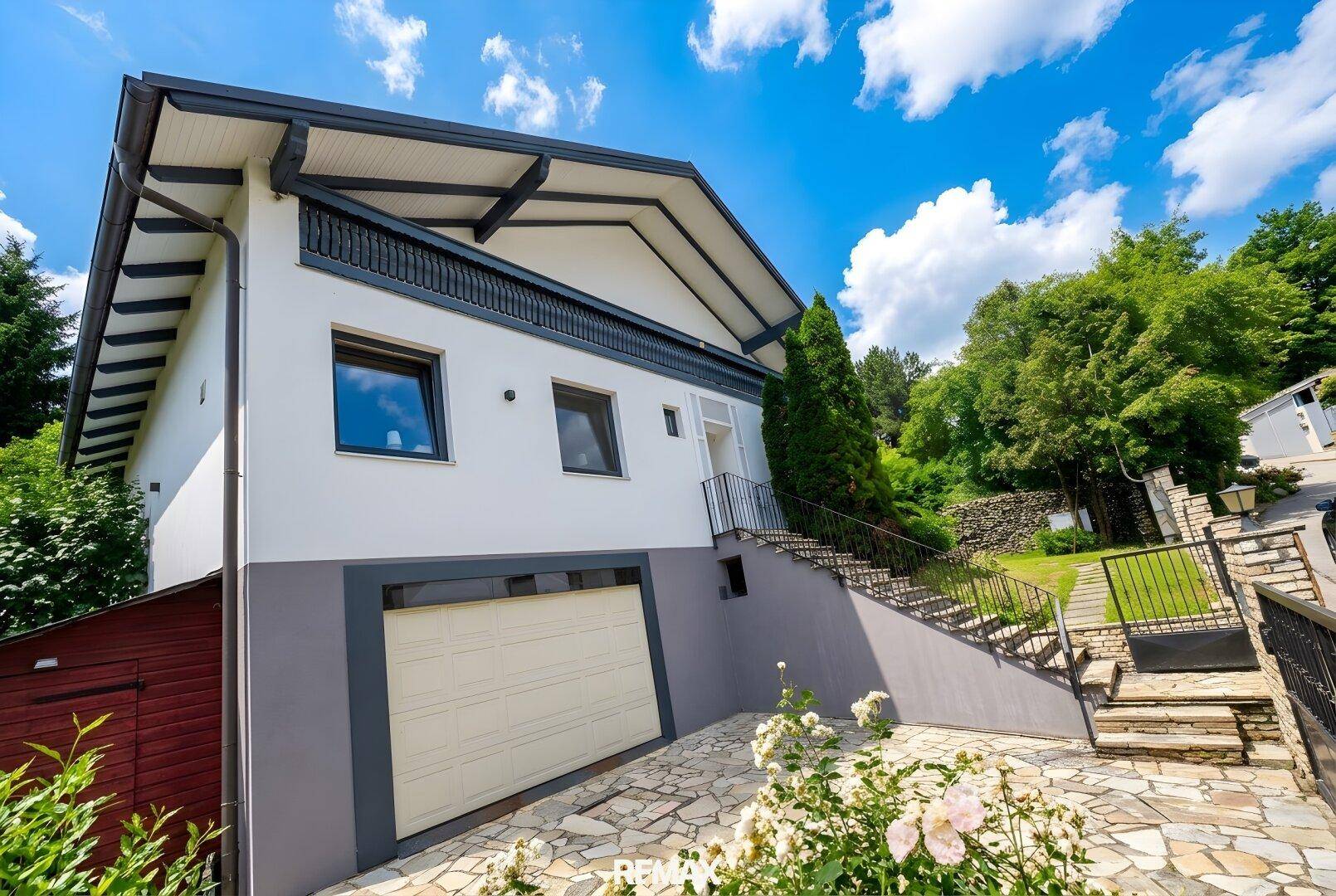 Modernes Haus mit Garage, Außentreppe und gepflegtem Vorgarten mit blühenden Rosen.