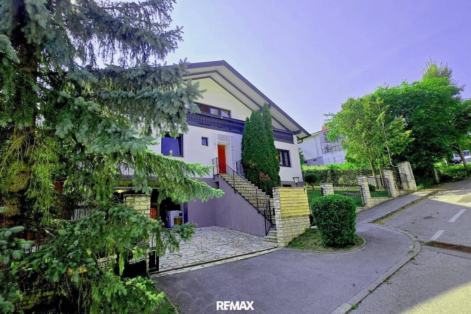 Ansicht des Hauses von der Straße mit Garage, Außentreppe und umgebender Vegetation.