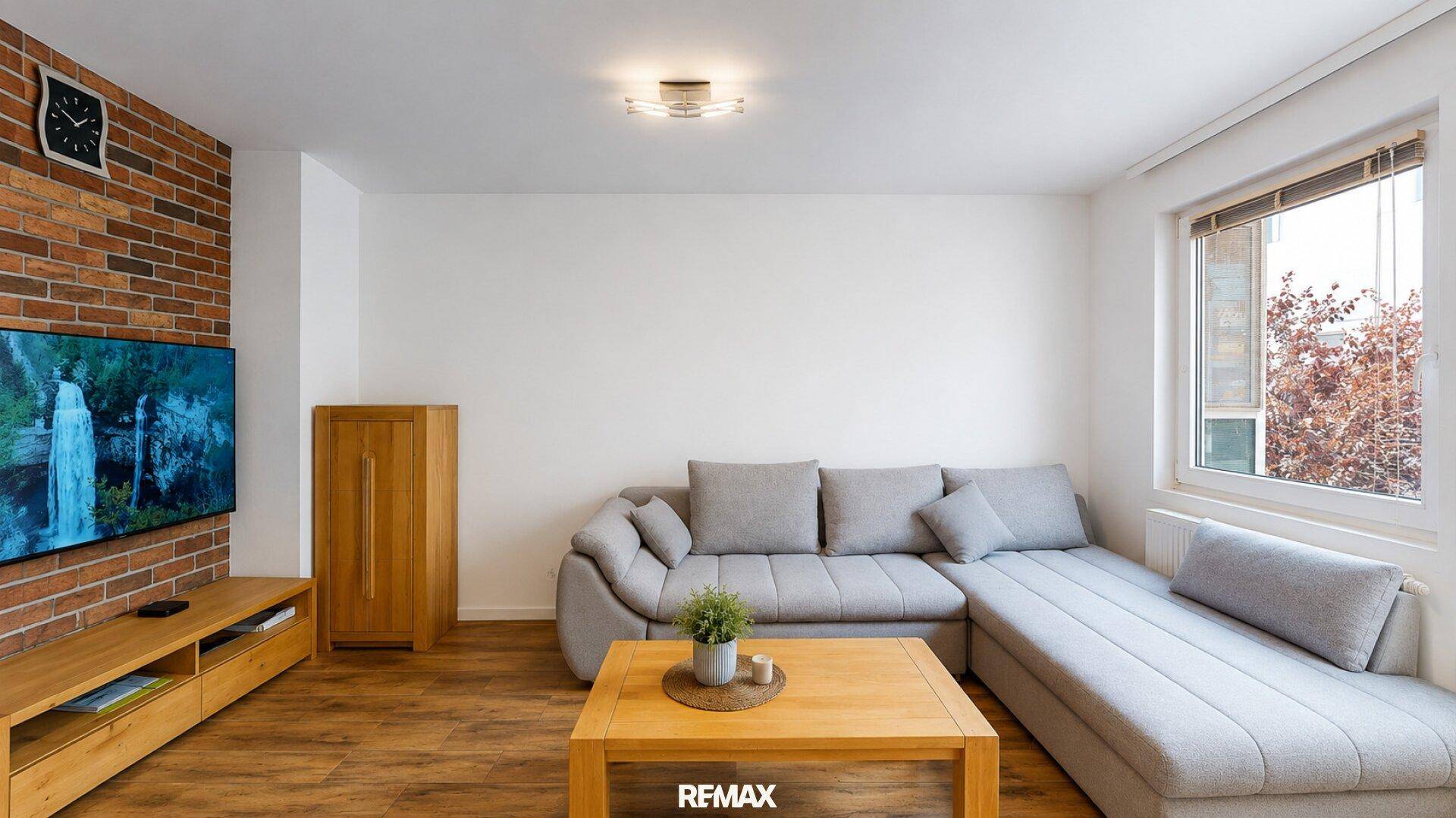 Gemütliches Wohnzimmer mit großem Ecksofa, Holzboden und einem Flachbildfernseher an der Ziegelwand.