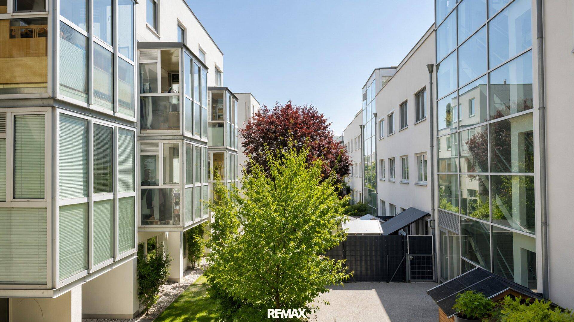 Moderne Wohnanlage mit Glasfassaden und begrüntem Innenhof, bietet eine angenehme Atmosphäre.