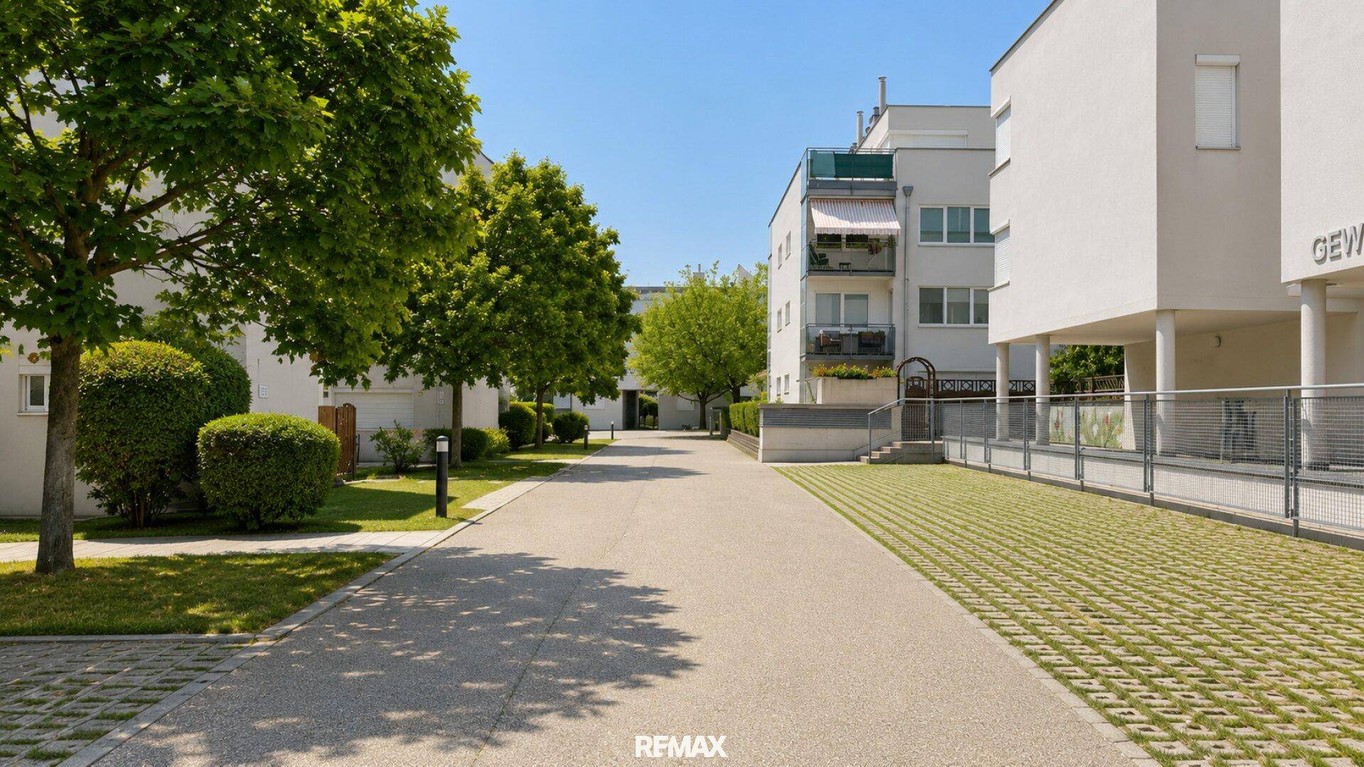 Zufahrtsweg zu einer modernen Wohnanlage mit Bäumen und begrünten Parkflächen.