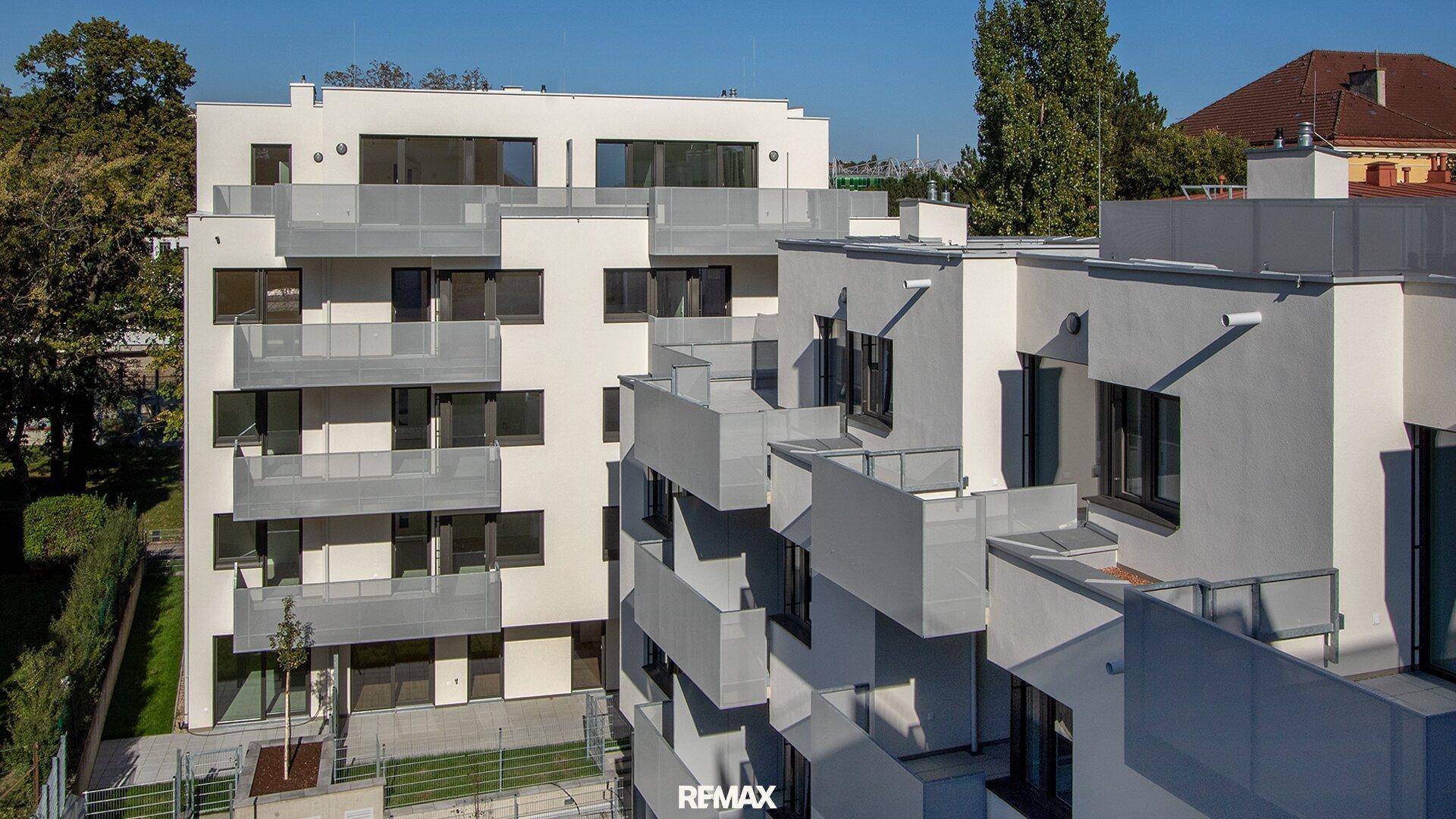 Moderne Wohnanlage mit weißer Fassade, zahlreichen Balkonen und großen Fenstern, umgeben von Grün.