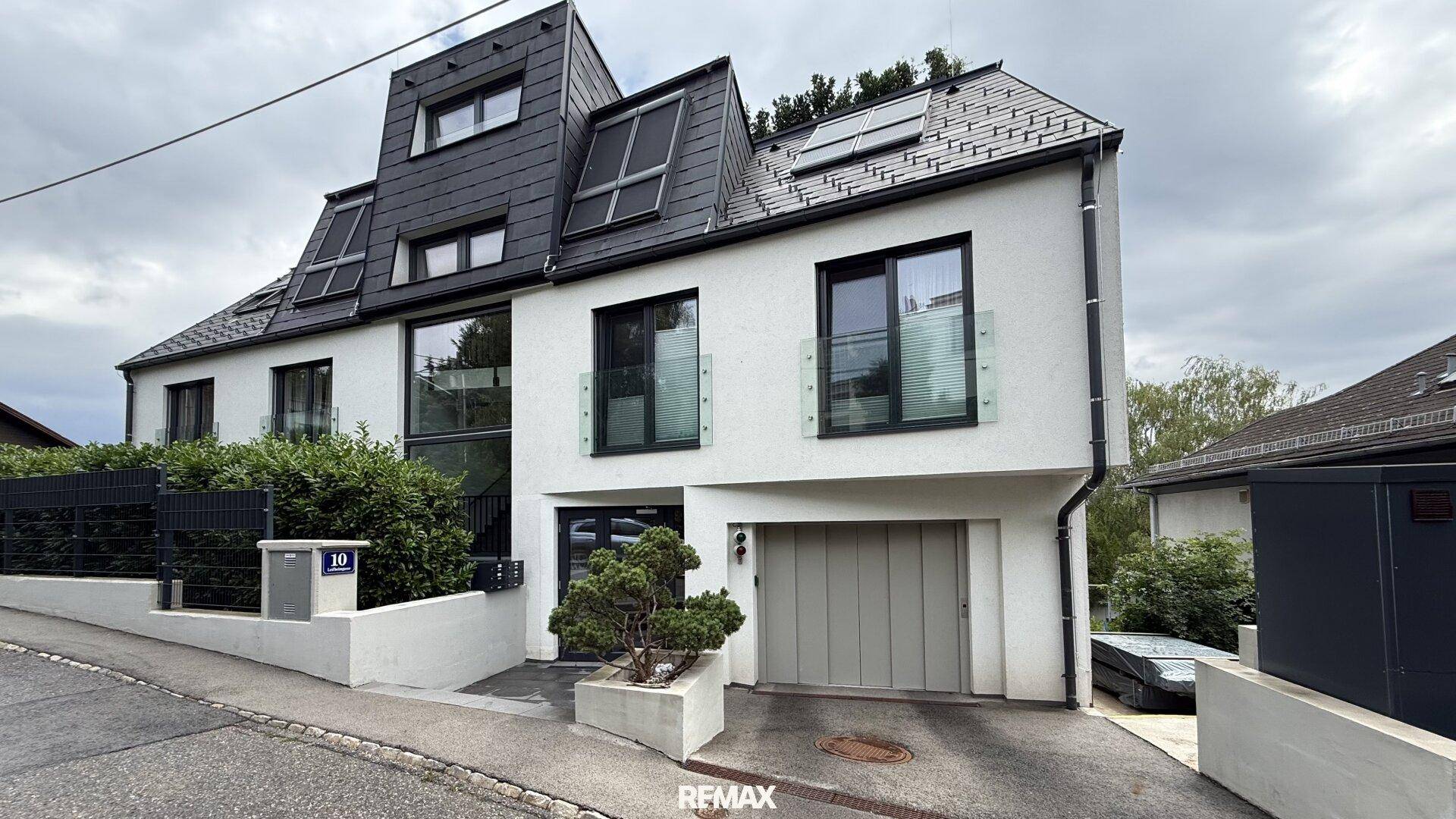 Moderne Wohnhausfassade mit mehreren Etagen, großen Fenstern und integrierter Garage.