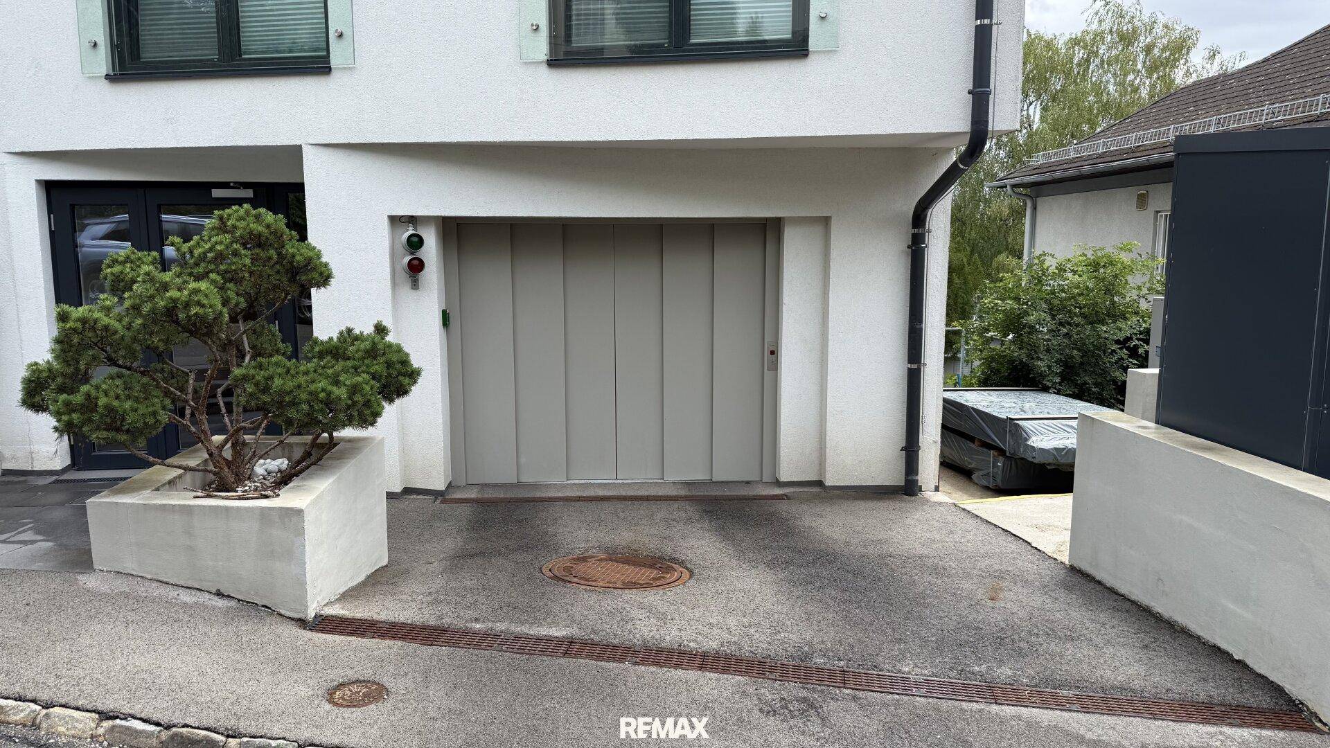 Eingangsbereich der Garage mit Zufahrt und kleiner Bepflanzung vor dem modernen Gebäude.