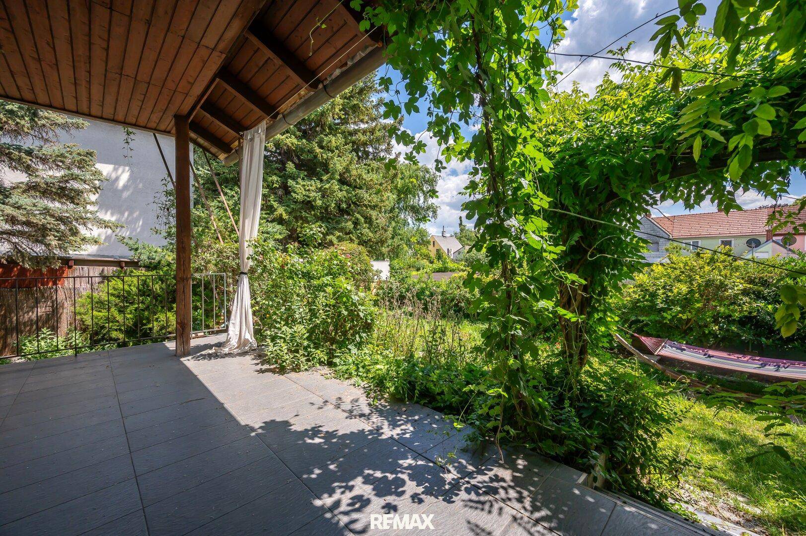 Überdachte Terrasse mit Fliesenboden und Blick auf den grünen Garten.