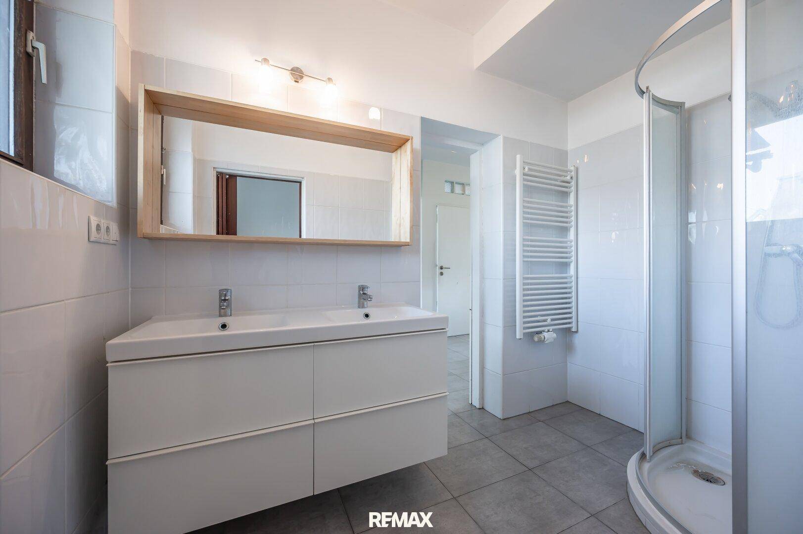 Modernes Badezimmer mit Doppelwaschbecken, Duschkabine und beheiztem Handtuchhalter.