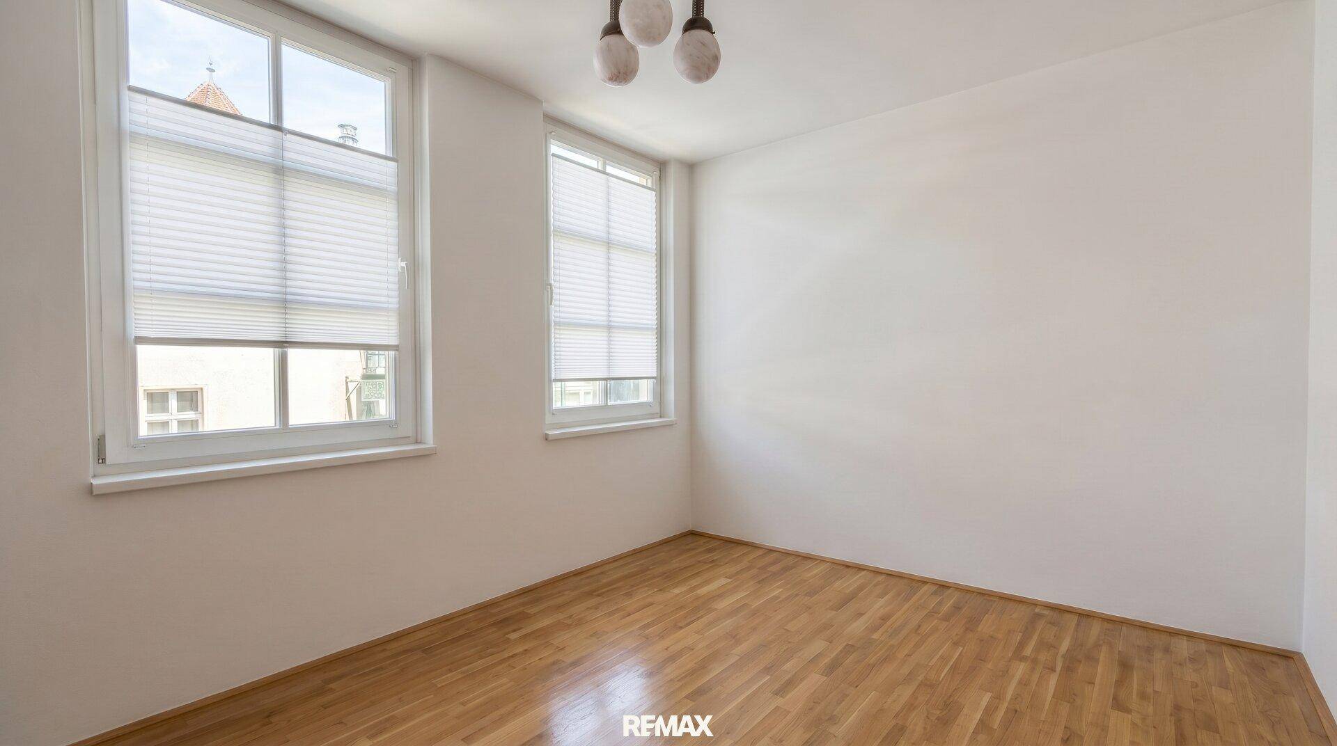 Geräumiges Schlafzimmer mit Holzboden und großen Fenstern, die viel Tageslicht hereinlassen.