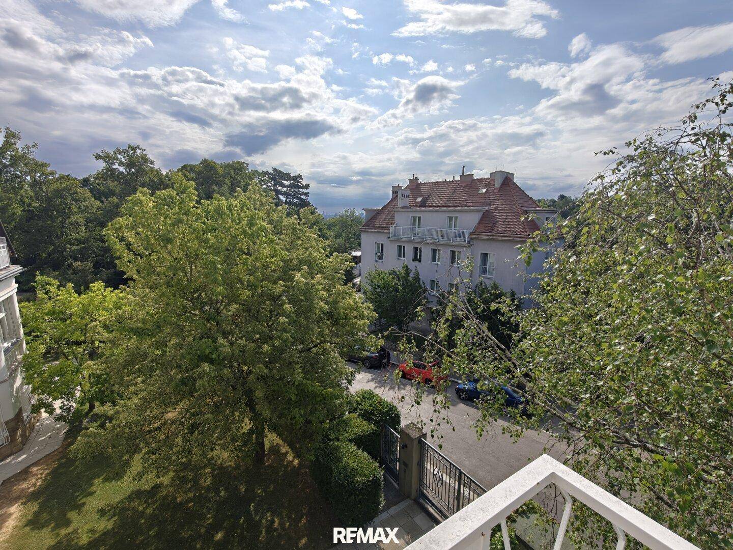 Blick vom Balkon auf die grüne Umgebung und die umliegenden Gebäude unter bewölktem Himmel.