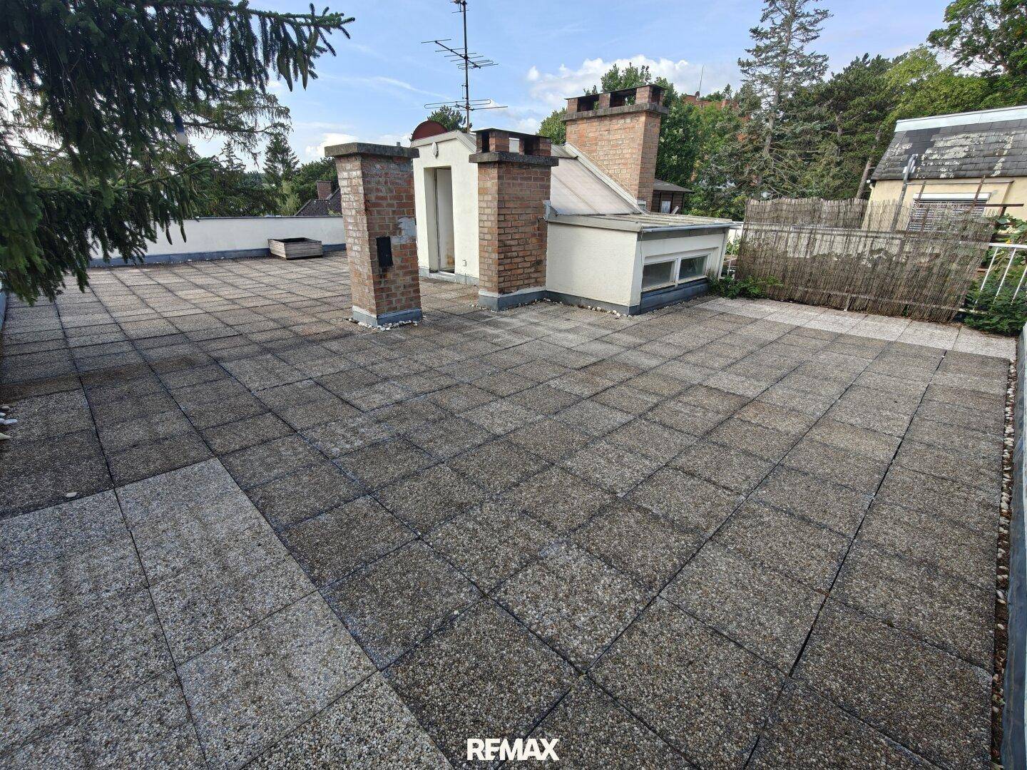Große, geflieste Dachterrasse mit Schornsteinen und Blick auf die umliegenden Dächer und Bäume.