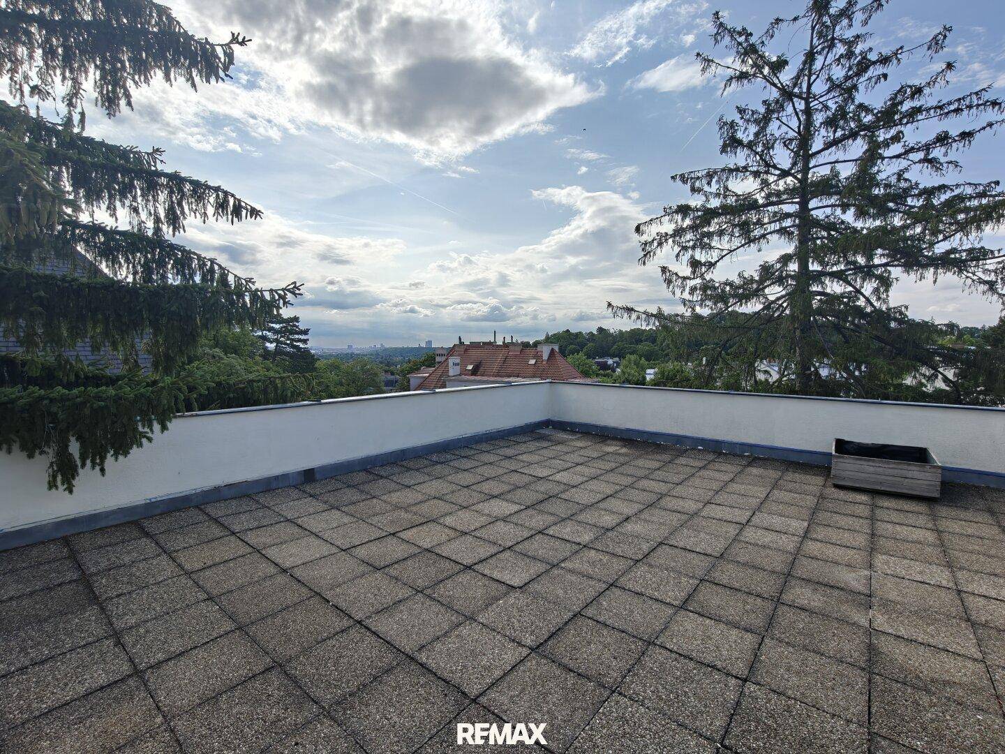 Weitläufige Dachterrasse mit Fliesenboden und Panoramablick auf die Stadt und die grüne Umgebung.
