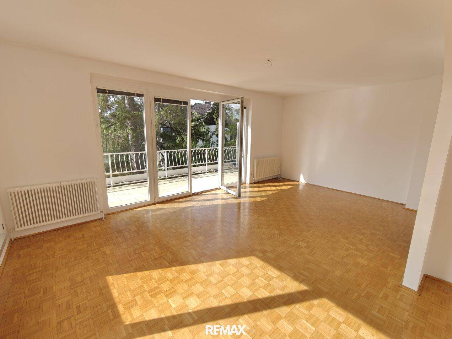 Helles, leeres Wohnzimmer mit Parkettboden und Zugang zu einem Balkon, ideal für individuelle Gestaltung.