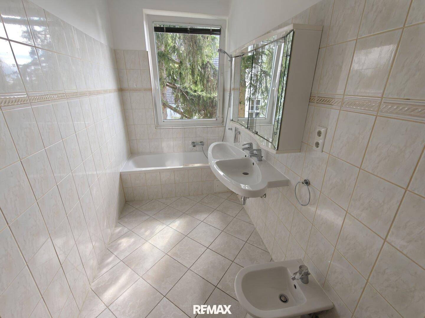 Helles Badezimmer mit Badewanne, Waschbecken, Bidet und Fliesen an Wänden und Boden.
