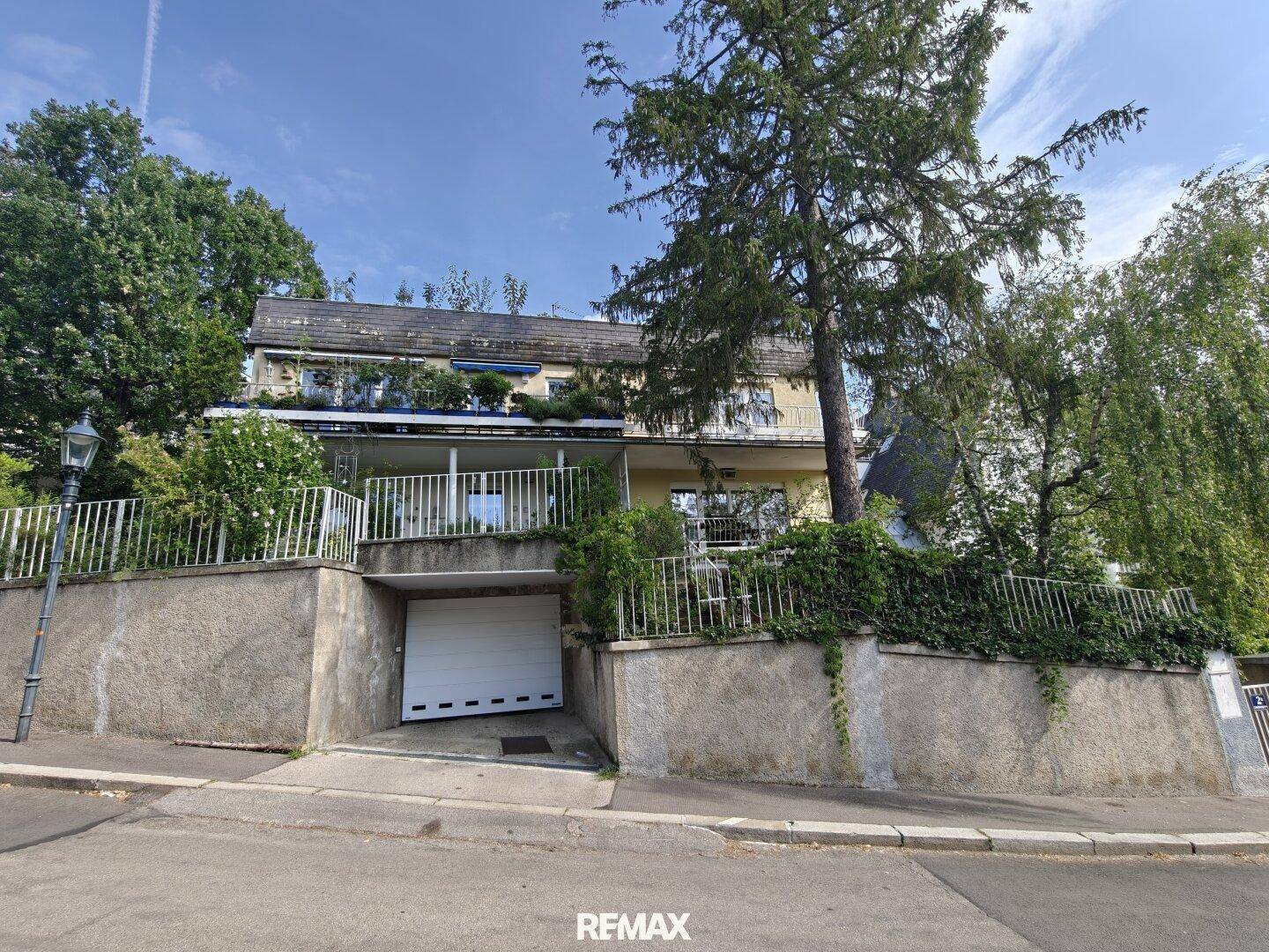 Außenansicht eines Hauses mit integrierter Garage und üppiger Vegetation an der Fassade.