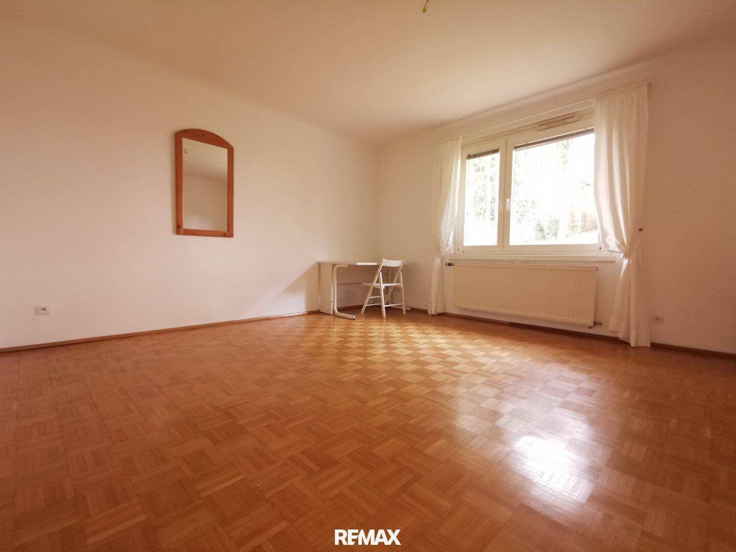 Leeres Wohnzimmer mit Fischgrätparkett und viel Tageslicht.