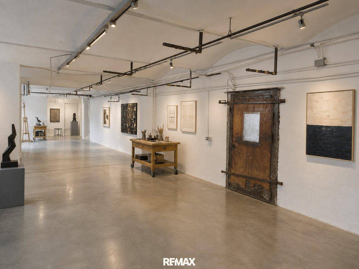 Langer Flur oder Ausstellungsbereich mit Betonboden, weiß gestrichenen Wänden und Kunstwerken.