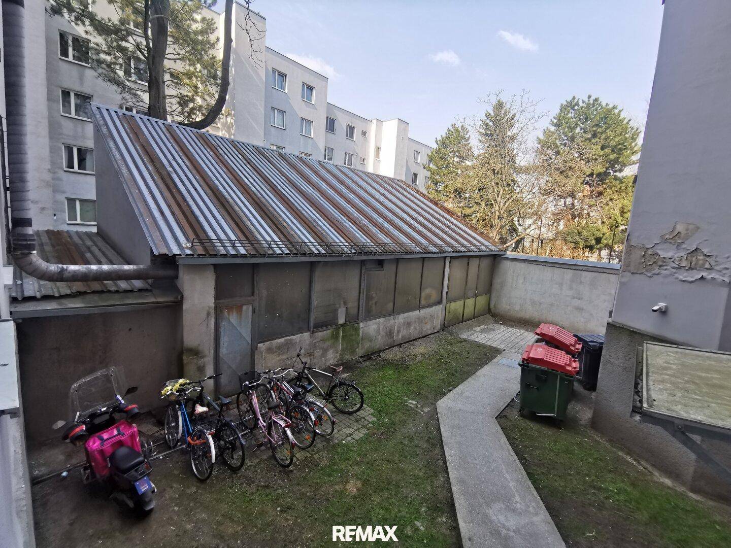 Hinterhofbereich mit Fahrradabstellplätzen, Mülltonnen und einem Gebäude mit Wellblechdach.