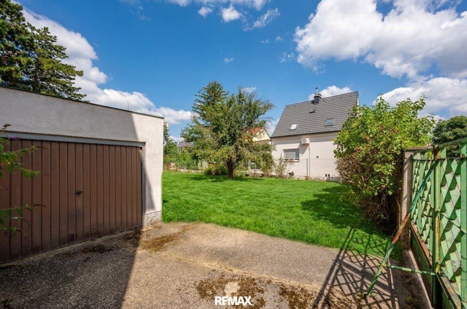 Garage mit braunem Tor und Betonweg, angrenzend an die grüne Rasenfläche des Grundstücks.