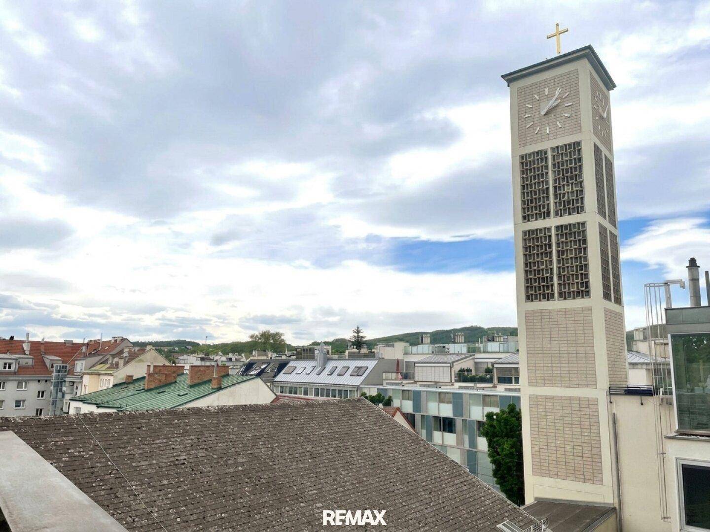 Dachlandschaft einer Stadt mit einem markanten Kirchturm unter bewölktem Himmel.