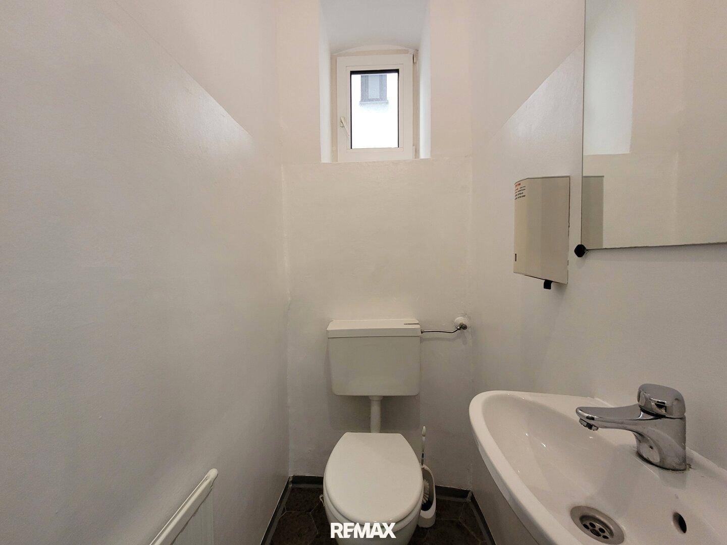 Kleines Gäste-WC mit Toilette, Waschbecken, Spiegel und einem kleinen Fenster für natürliche Belüftung.