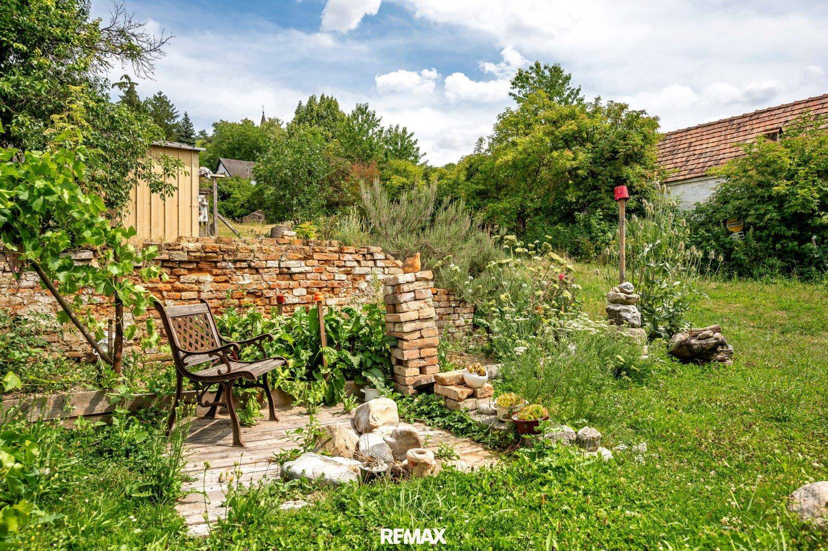 Rustikaler Sitzplatz im Garten mit einer alten Ziegelmauer und üppiger Bepflanzung.