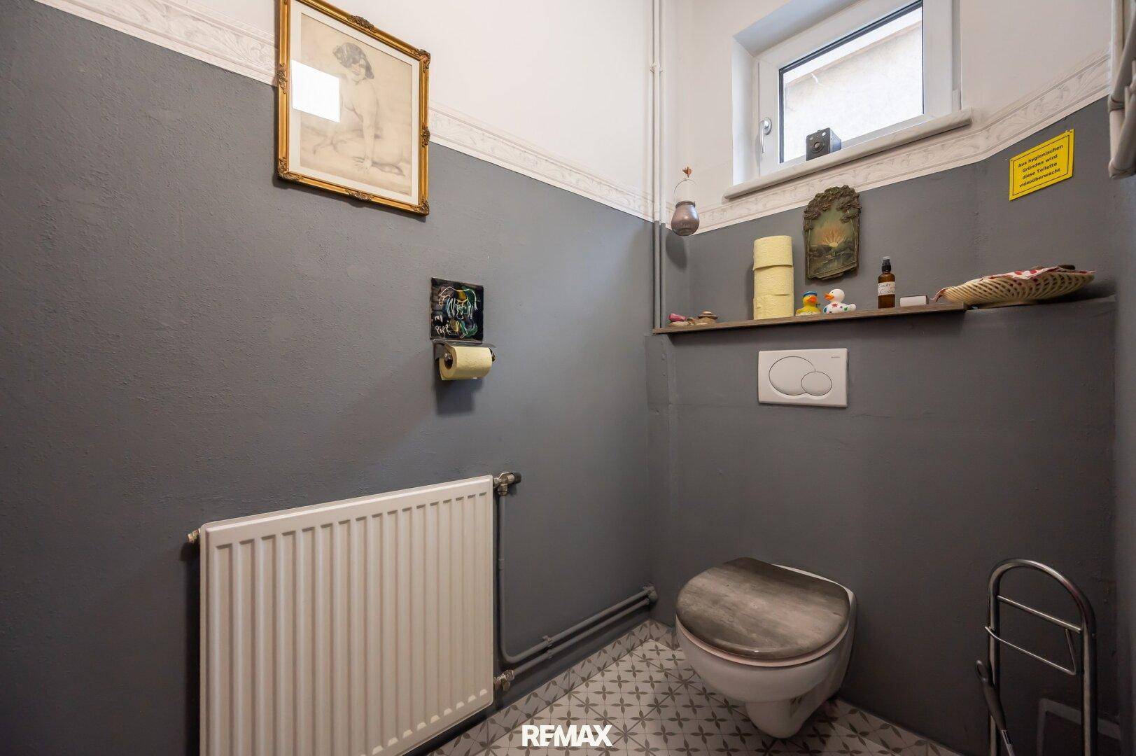 Kleines Gäste-WC mit grauen Wänden, Wand-WC und einem Fenster für Tageslicht.
