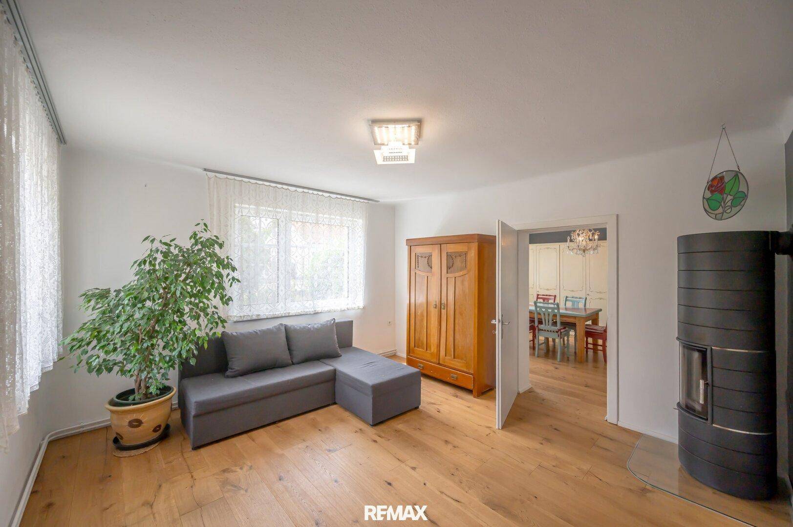 Gemütliches Wohnzimmer mit Holzboden, Sofa und einem Kaminofen, offen zum Essbereich.