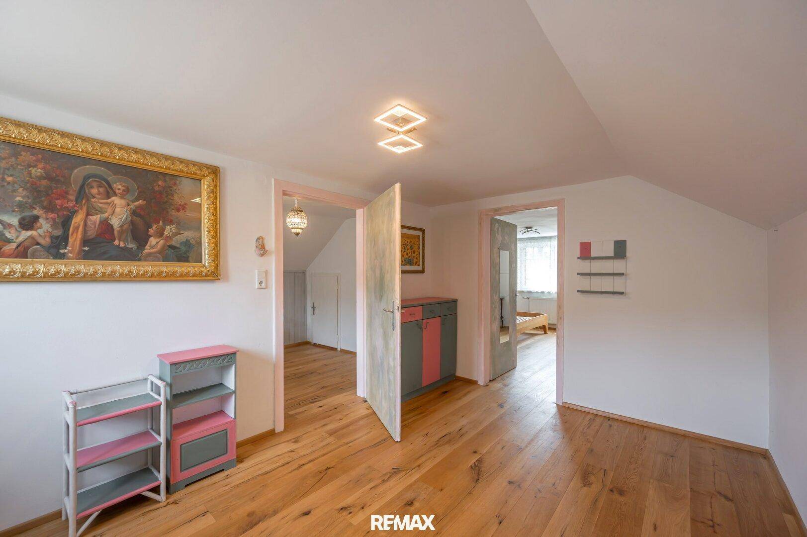 Dachgeschosszimmer mit Holzboden und Dachschräge, das mehrere Türen zu anderen Räumen bietet.