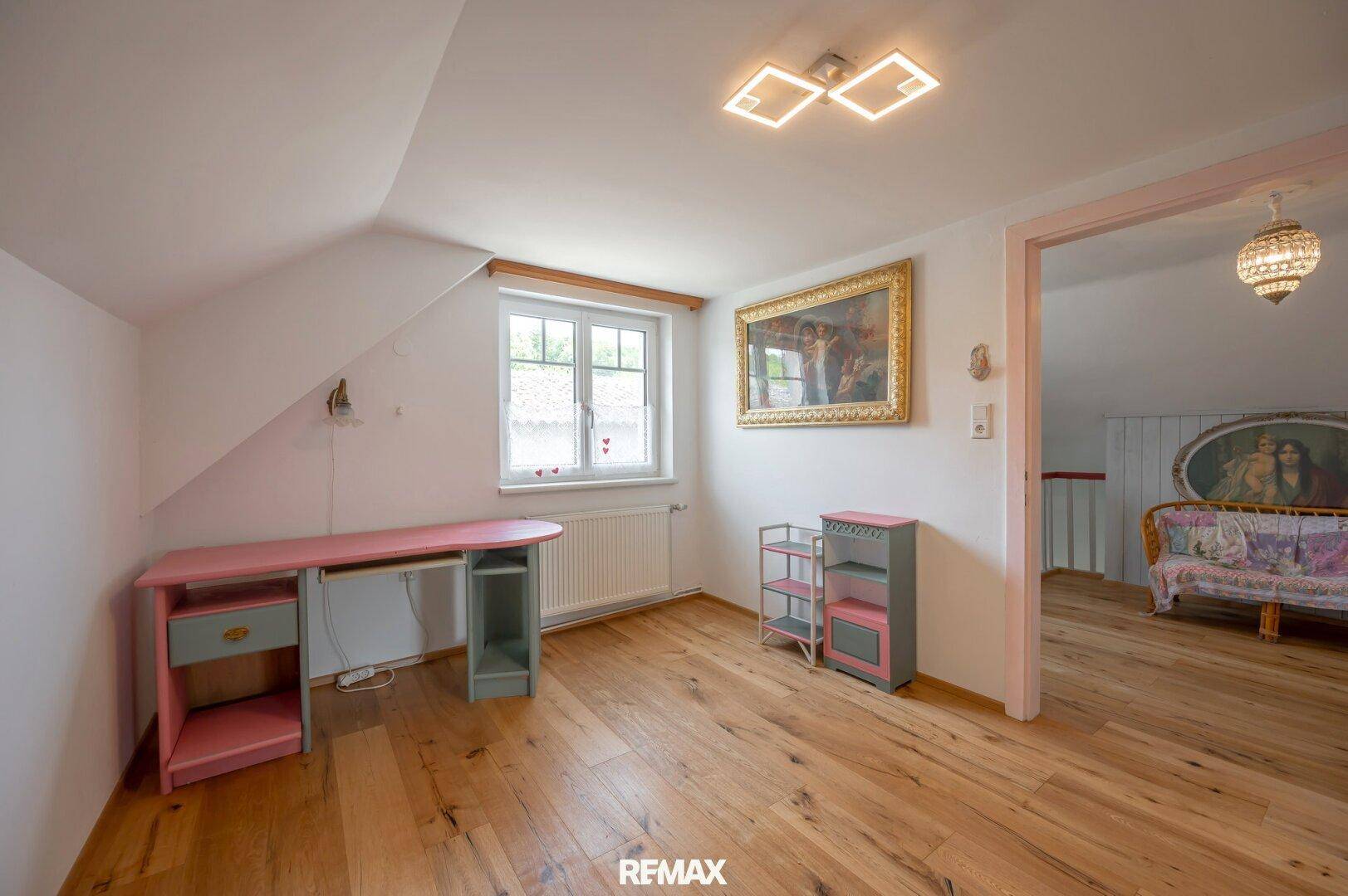 Helles Dachgeschosszimmer mit Holzboden, Schreibtisch und Dachschräge, ideal als Arbeitszimmer.