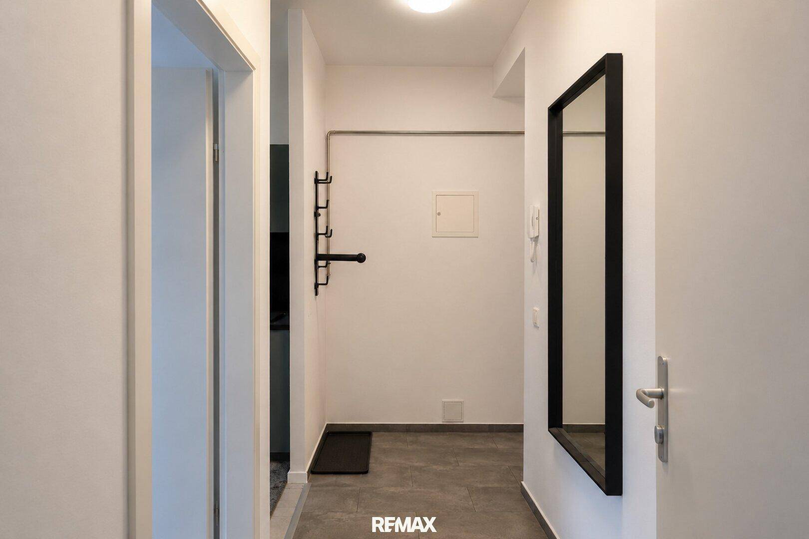 Schmaler Flur mit einem hohen Wandspiegel und einer praktischen Garderobe an der weißen Wand.