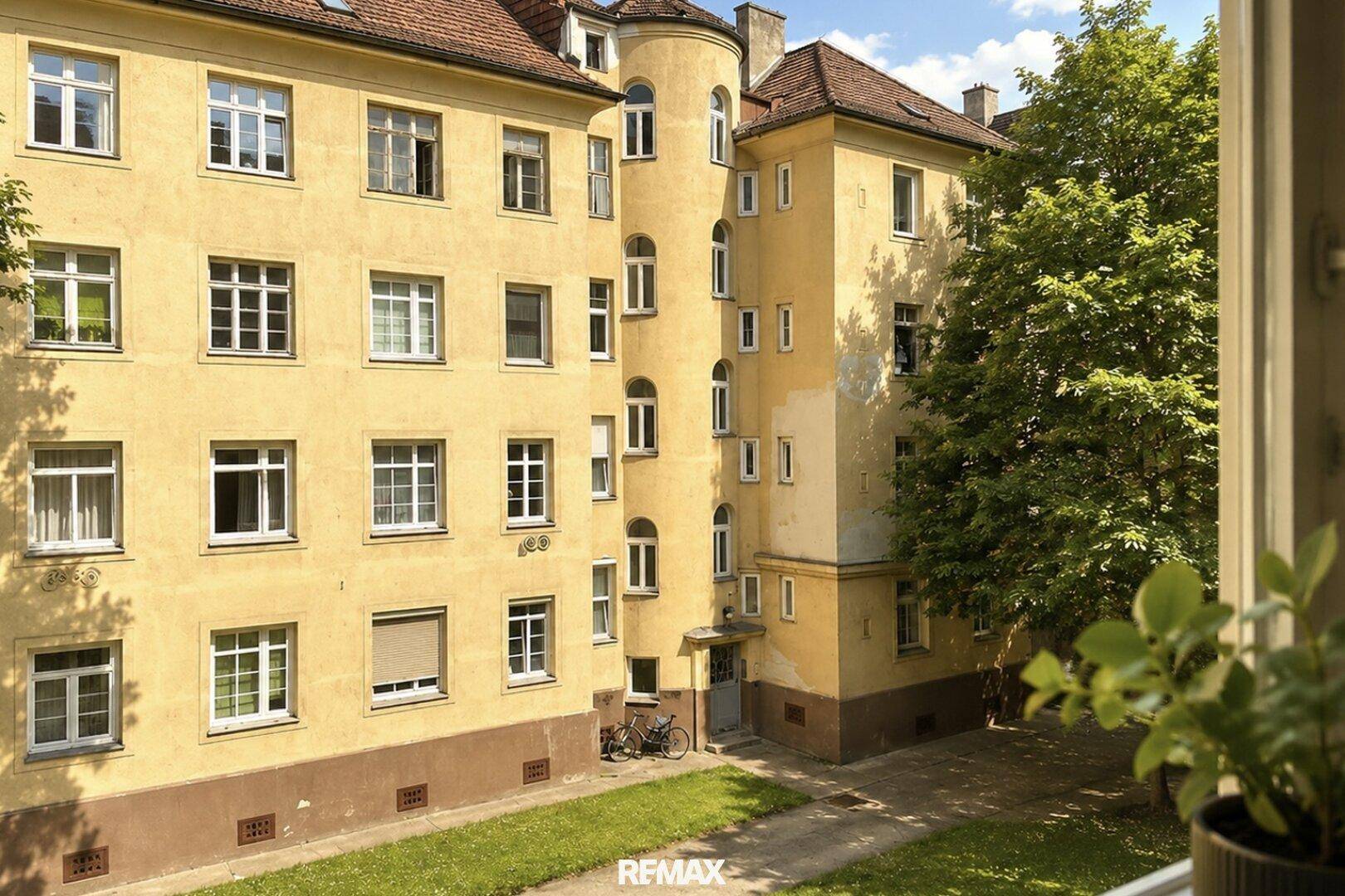 Historisches Mehrfamilienhaus mit gelber Fassade, vielen Fenstern und einem grünen Innenhof.