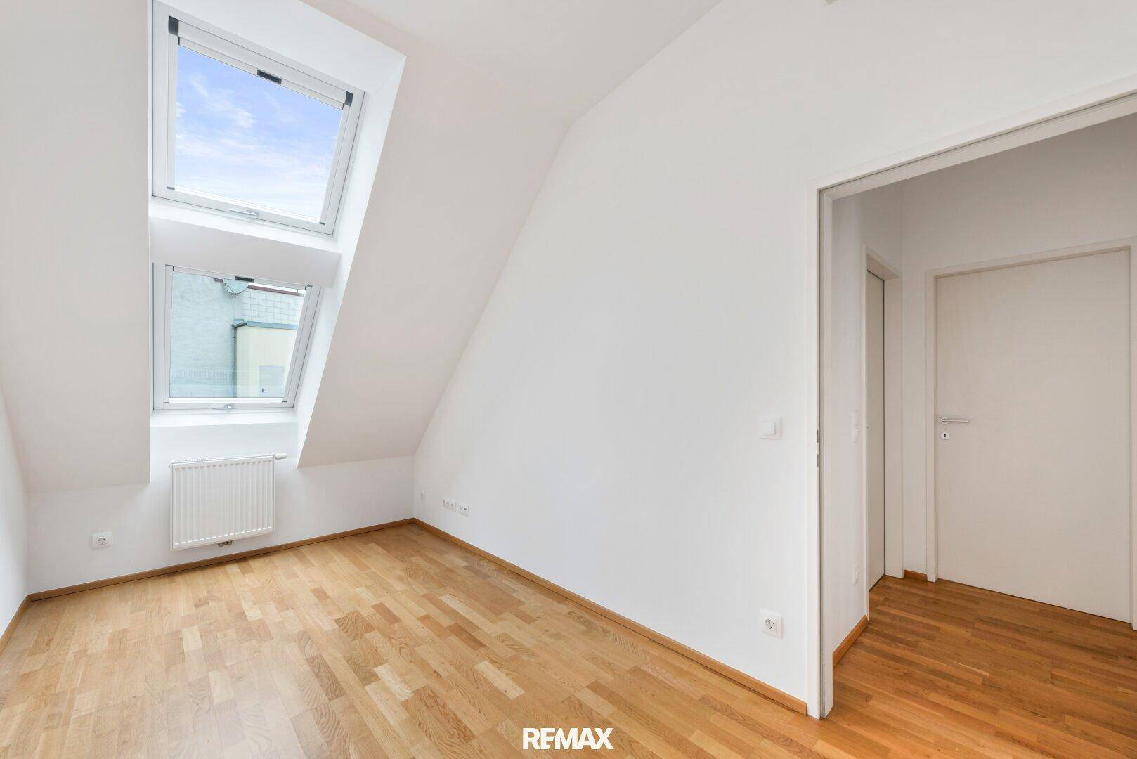 Helles Zimmer im Dachgeschoss mit Holzboden und zwei Dachfenstern.