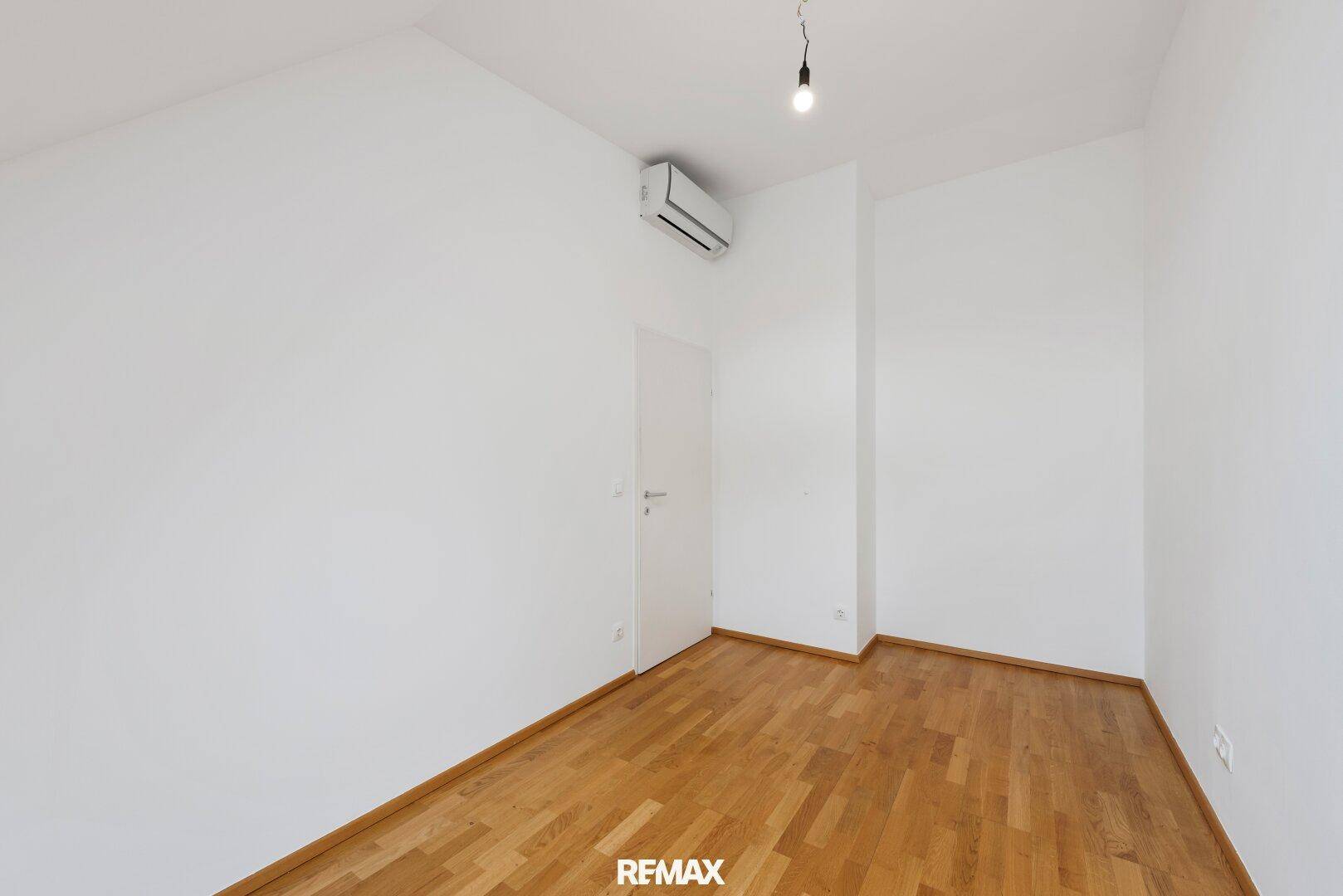 Geräumiges Zimmer mit Parkettboden, Klimaanlage und weiß gestrichenen Wänden.
