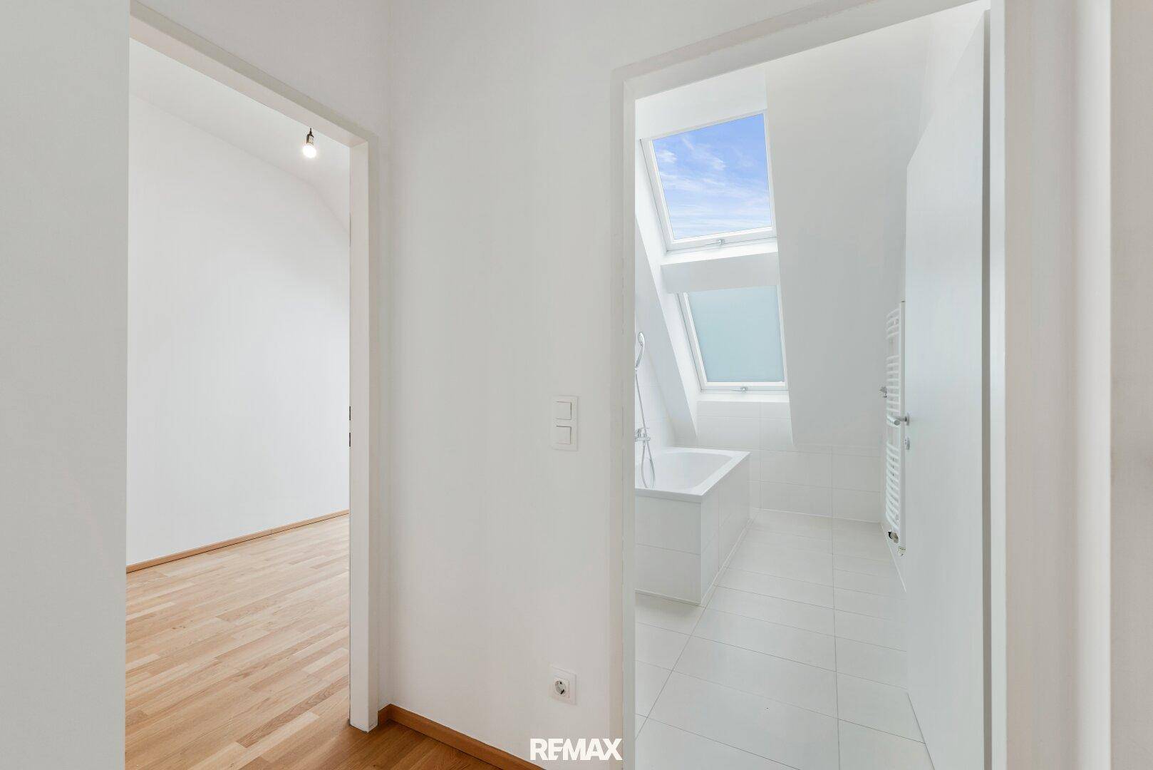 Heller Flur mit Zugang zu einem Badezimmer mit Dachfenstern und einem weiteren Raum.