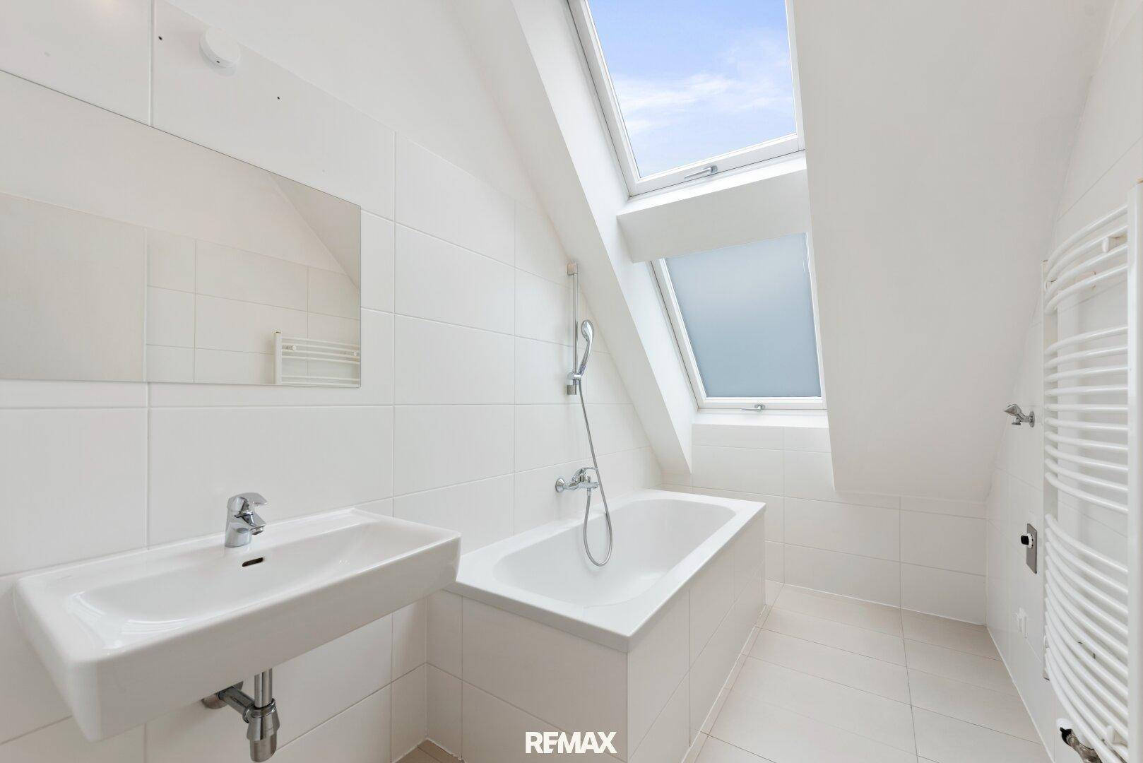 Modernes Badezimmer mit Badewanne, Waschbecken, Fliesen und Dachfenster.