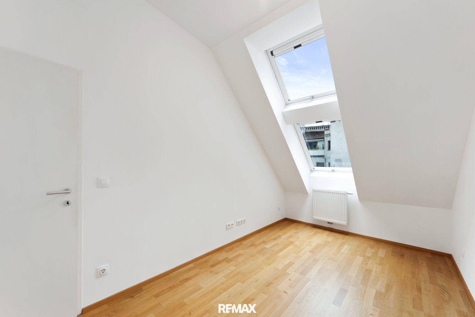 Helles Zimmer im Dachgeschoss mit Holzboden und zwei Dachfenstern.