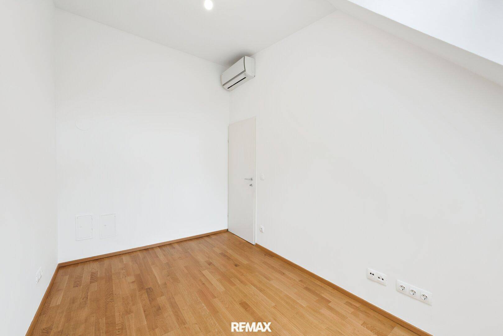 Geräumiges Zimmer mit Parkettboden, Klimaanlage und weiß gestrichenen Wänden.