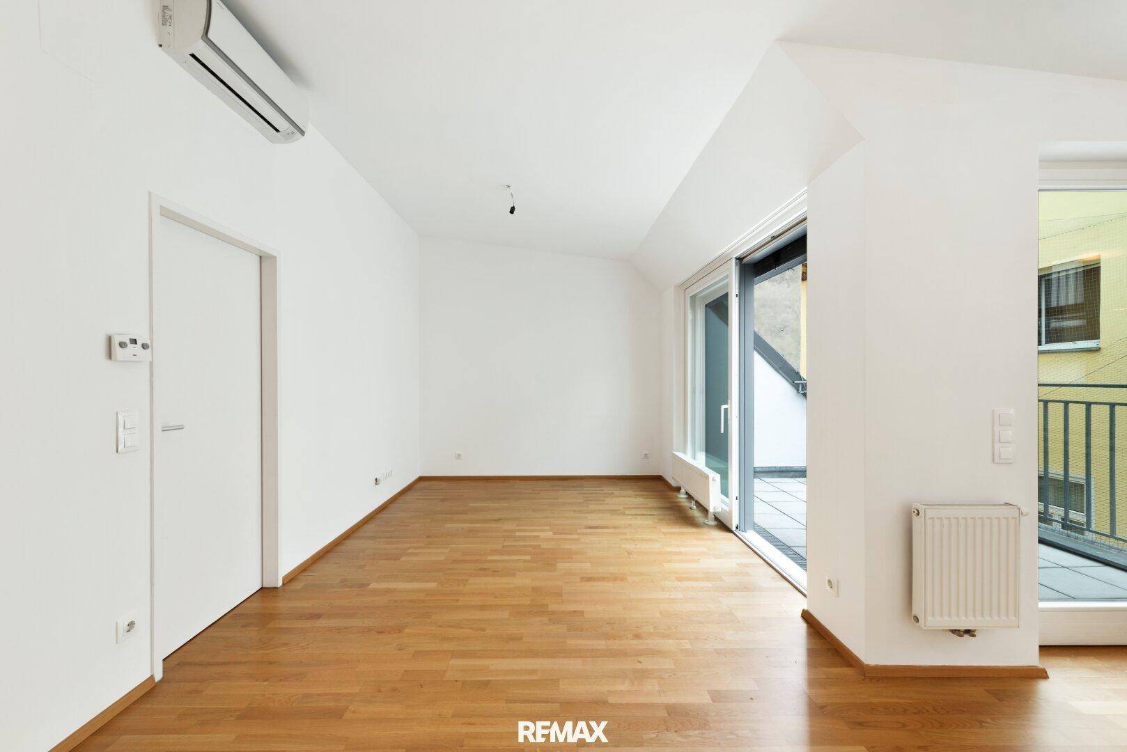 Heller Wohnbereich mit Parkettboden, Klimaanlage und Zugang zum Balkon.