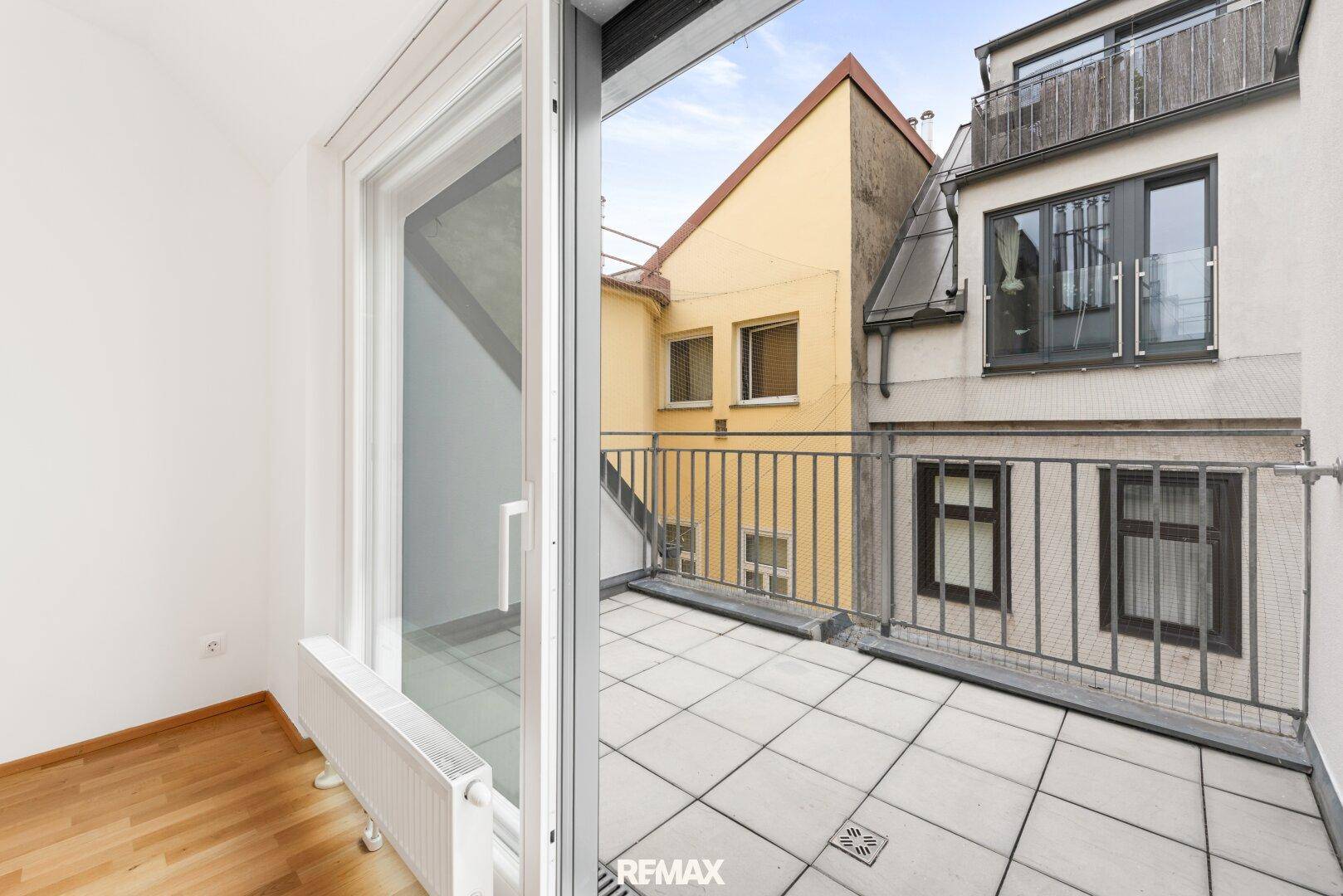 Kleiner Balkon mit Fliesenboden und Blick auf die umliegenden Gebäude.